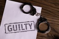 pexels-photo-6077431-6077431 Top view of handcuffs on paper with 'GUILTY' text, symbolizing a verdict or crime.